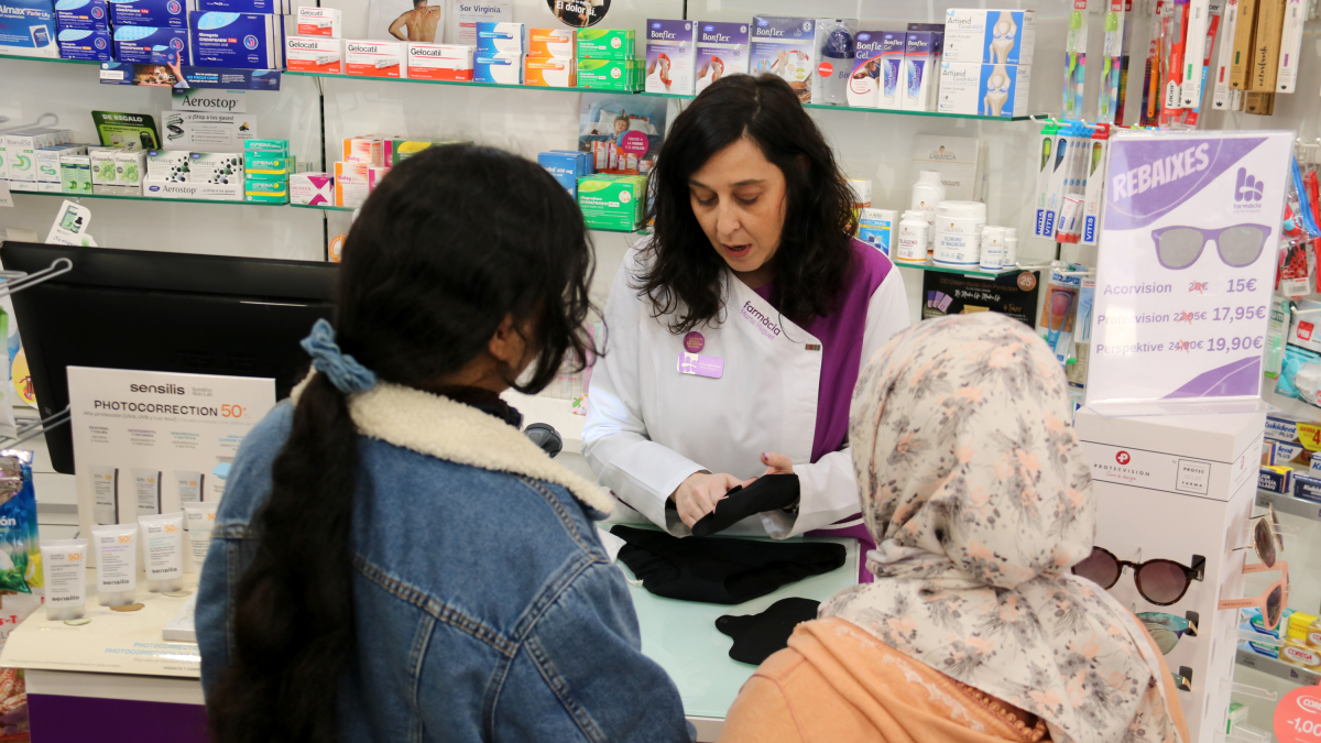 La farmacèutica Marta Huguet, de la farmàcia de Barbens, assessora dues dones sobre els productes menstruals reutilitzables