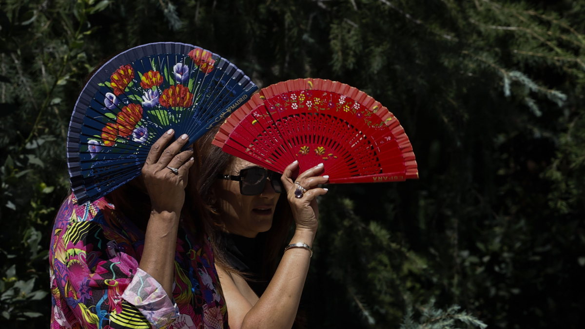 Dos mujeres se protegen del sol con abanicos y buscando la sombra de los árboles en el parque del Retiro en una imagen de archivo.