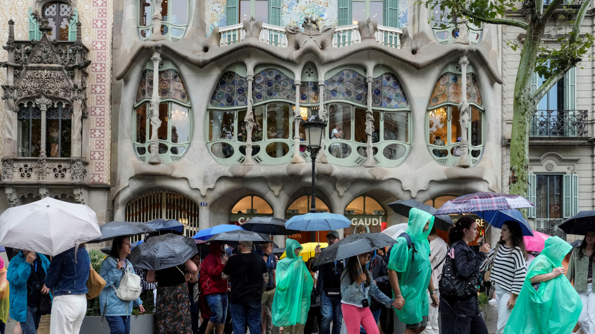 Fotografia d’arxiu de diversos turistes protegint-se de la pluja als voltants de la Casa Batlló del passeig de Gràcia de Barcelona.