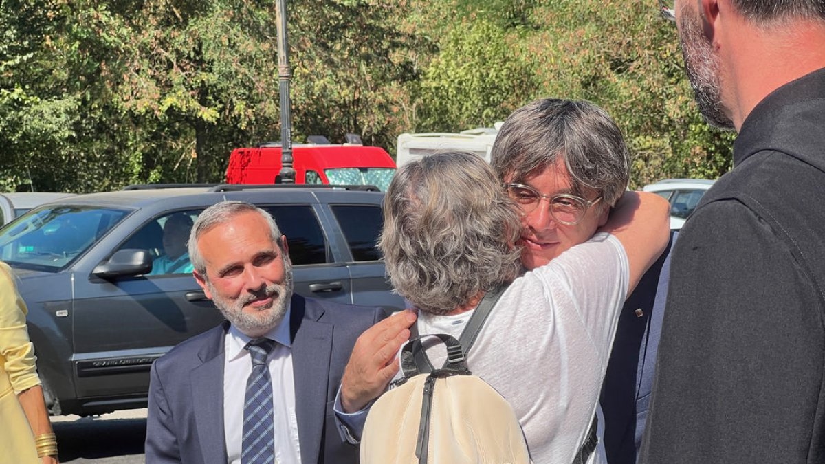 Carles Puigdemont abraza a una militante en la llegada a un acto acompañado de Josep Lluís Alay. - ACN