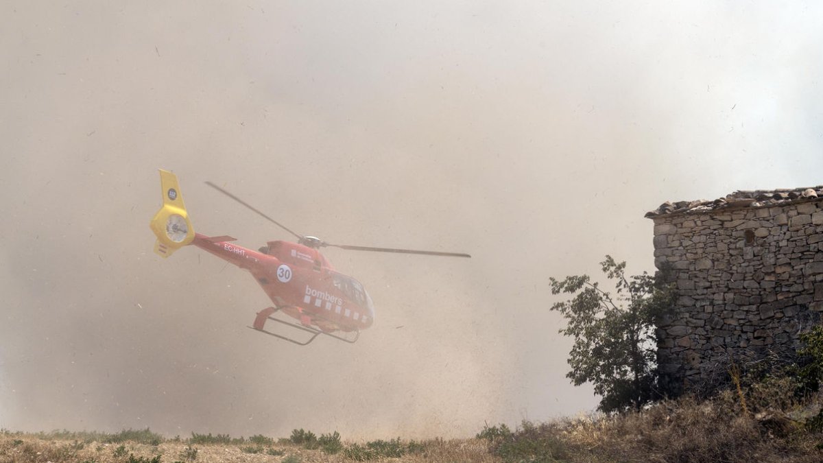 Un helicóptero de los Bomberos ante una densa columna de humo. - XAVIER SANTESMASSES