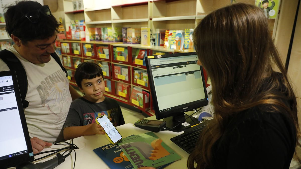 Un nen mostra al mòbil el val per comprar material escolar, ahir a la botiga Abacus de Lleida. - AMADO FORROLLA
