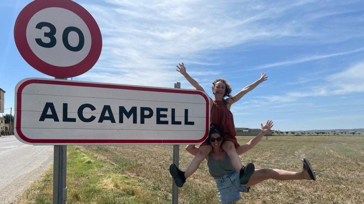 Dos membres de la Plataforma de Dones Artistes Rurals, al costat del cartell d’entrada d’aquesta localitat de la Llitera.