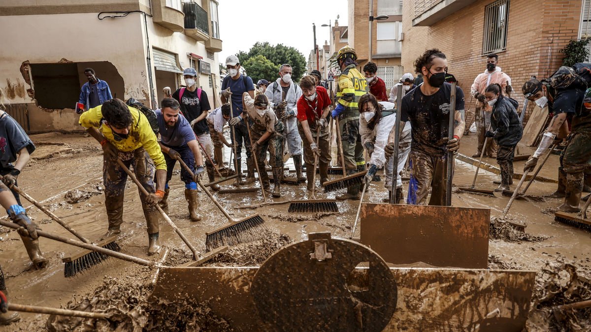 Voluntarios y equipos de emergencias limpian una calle de barro en Massanassa. - EFE
