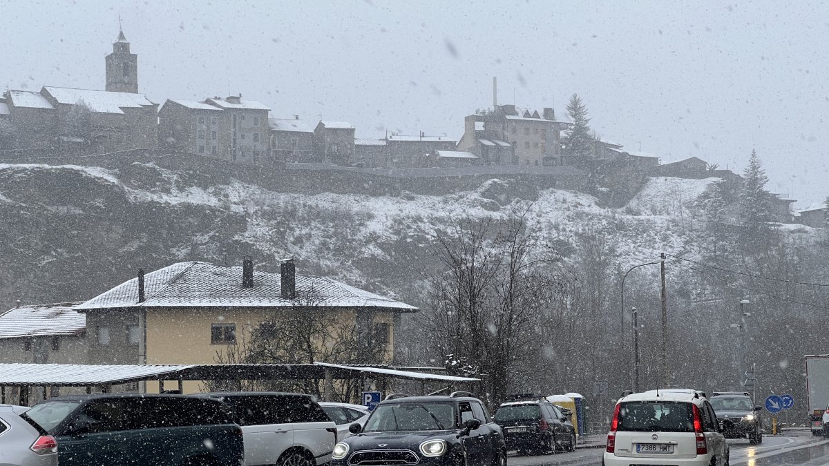 Vehicles circulant amb normalitat per l’N-260 i amb el poble de Bellver de Cerdanya tenyit de blanc per la neu al fons.