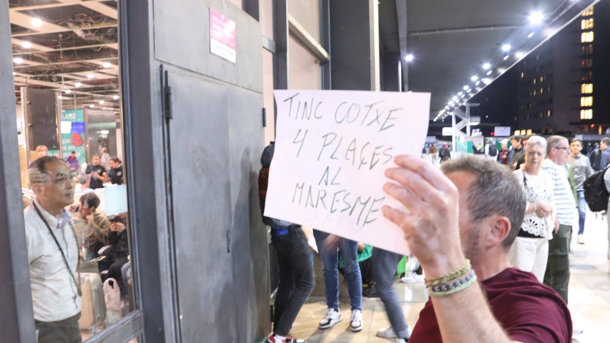 Un hombre con un cartel en que ofrece cuatro plazas al coche para ir al Maresme, delante de Sants de Barcelona
