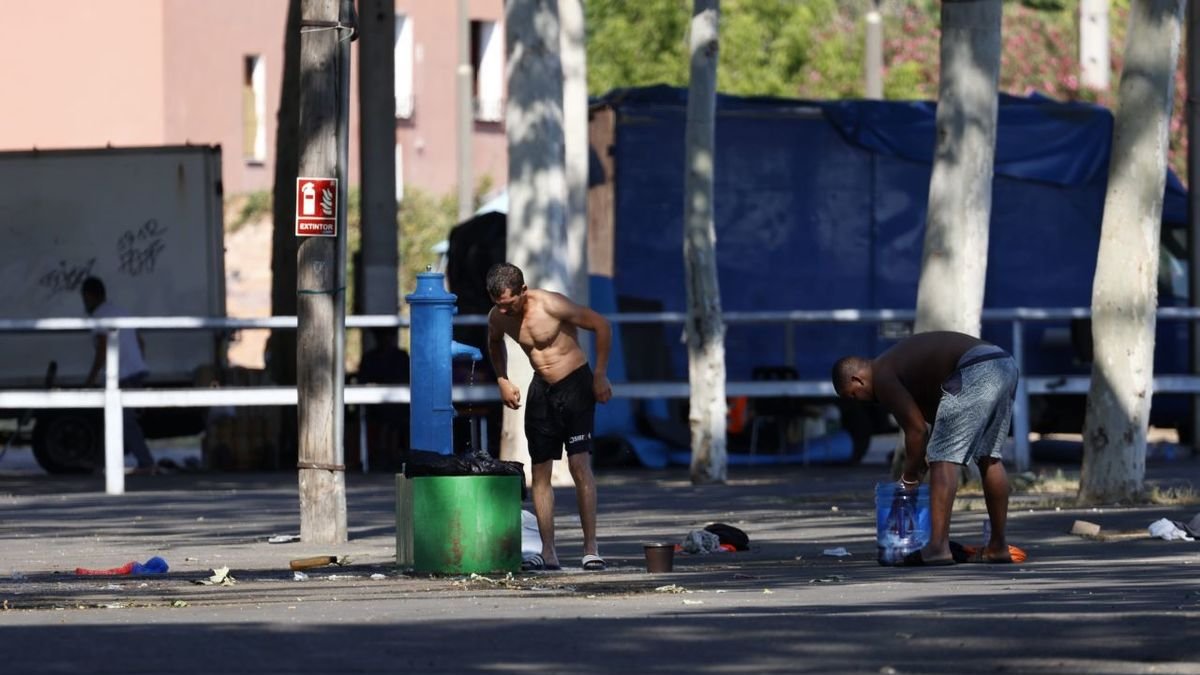 Dos personas aseándose en la fuente que han habilitado junto al pabellón 3 que hace de albergue. - JORDI ECHEVARRIA