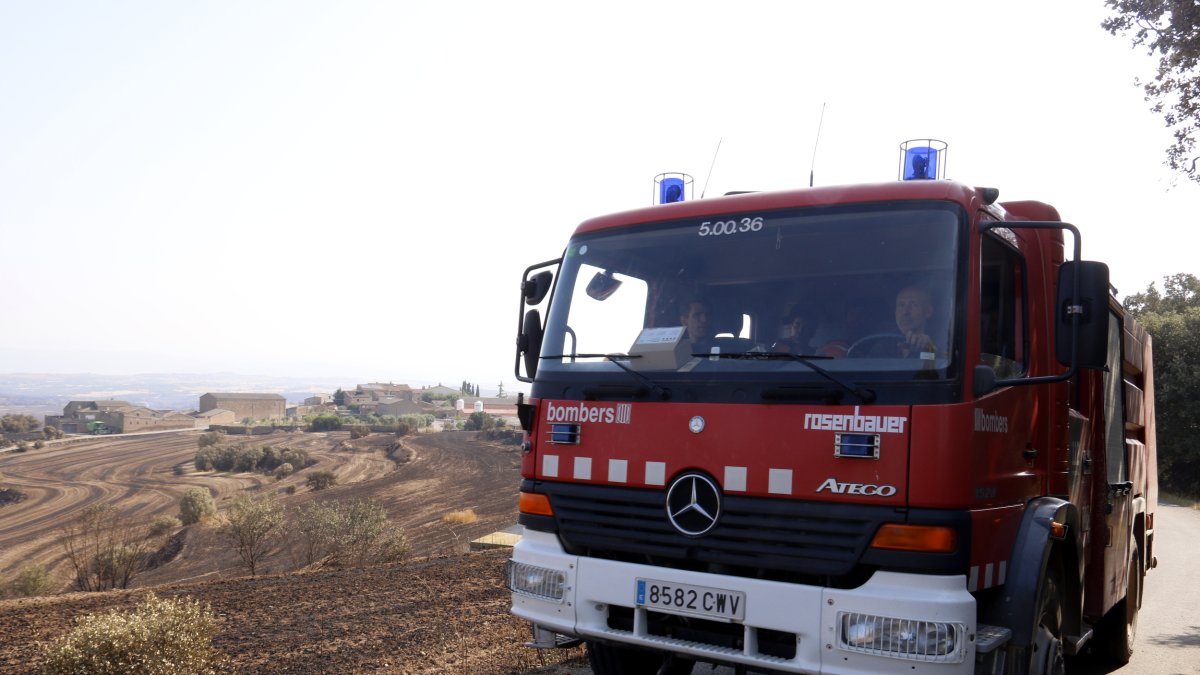Un camión de Bomberos a las proximidades del núcleo de Guardiola, al municipio de Vilanova de l'Aguda, con campos afectados por el incendio de Torrefeta en el fondo.