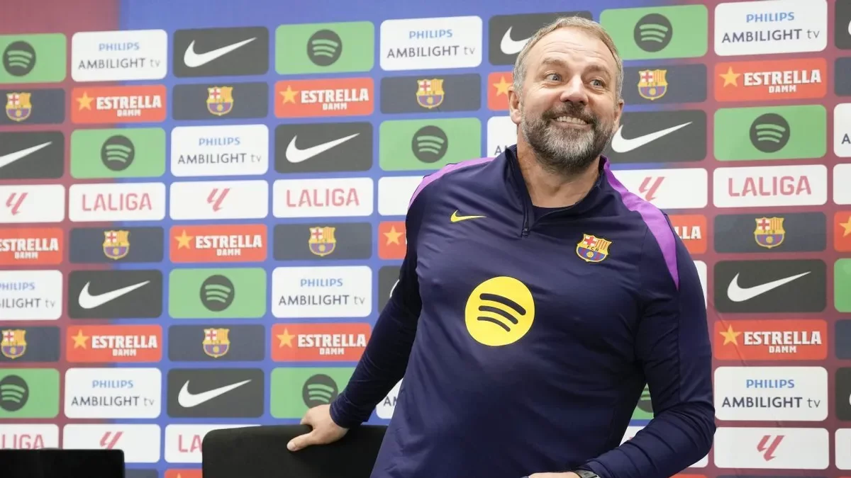 Hansi Flick, somrient mentre s’asseu a la sala de premsa.