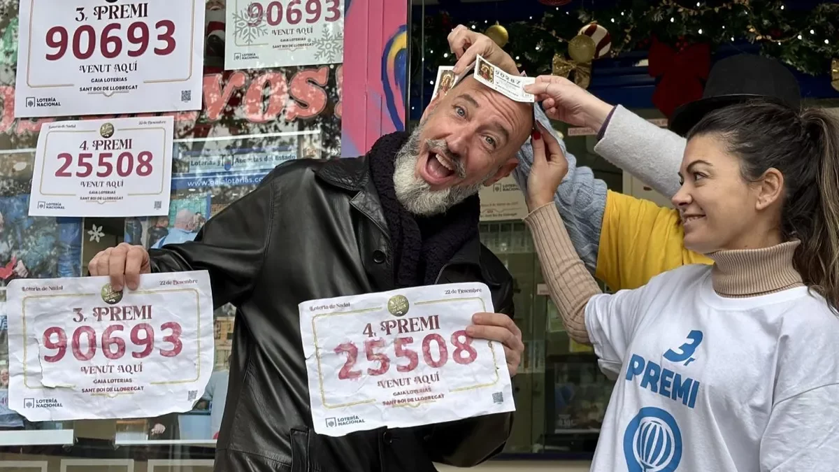 Raúl, el ‘calb de la sort’, subjectant els dos números premiats que van agraciar Sant Boi. - ACN / ALBERT SEGURA