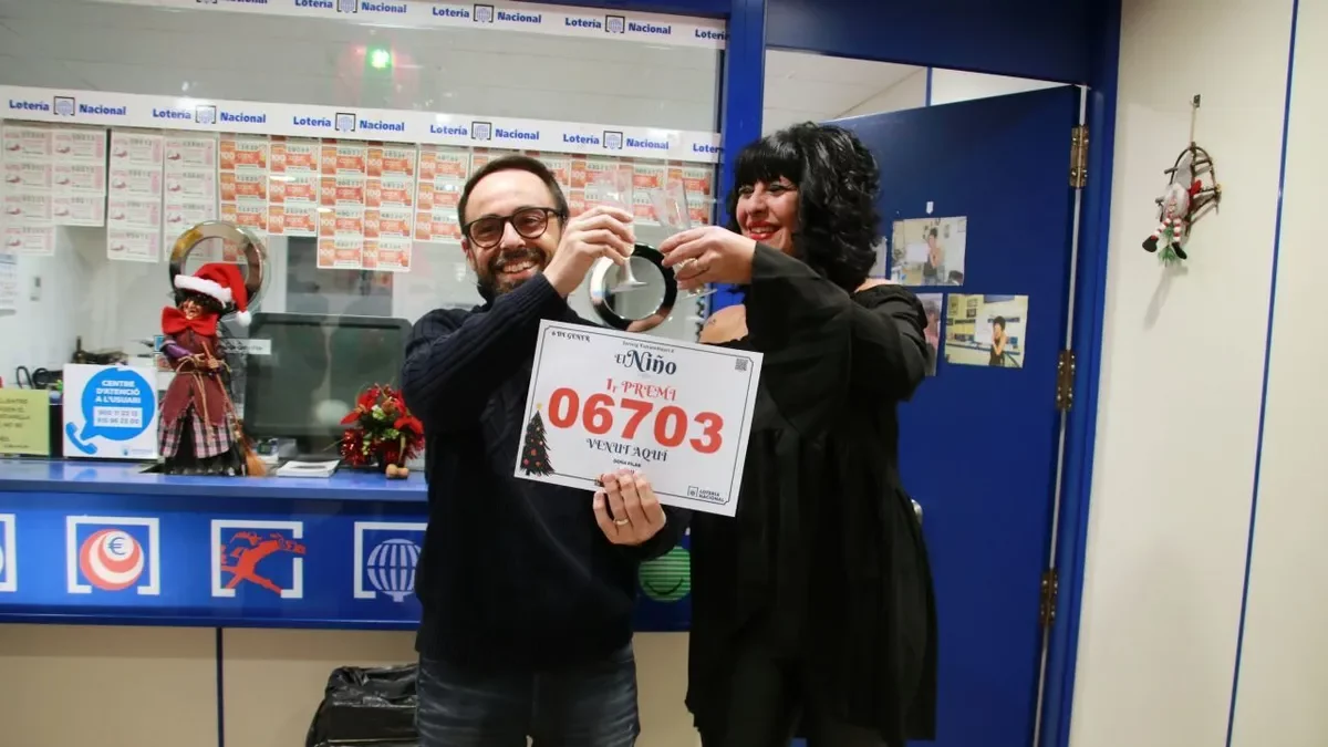 Dos treballadors de l’administració Doña Pilar de Salou, ahir amb el cartell del primer premi. - ACN / MAR ROVIRA