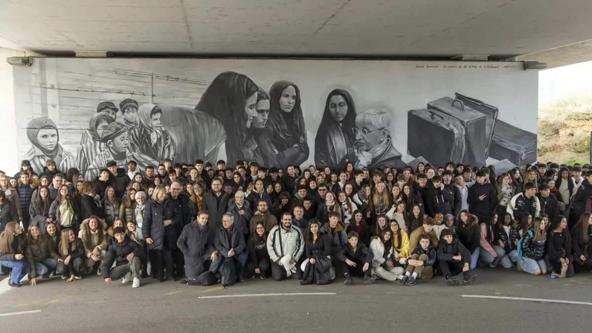 Fotografia de família amb estudiants, i Teresa Curià al centre, davant del mural commemoratiu (de 14 metres de llarg per cinc d’alt), sota el pont de Príncep de Viana. - JAUME SANS/PAERIA