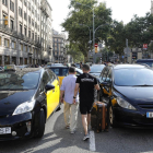 Varios turistas pasan entre los taxis que ocupan la Gran Vía de Barcelona.
